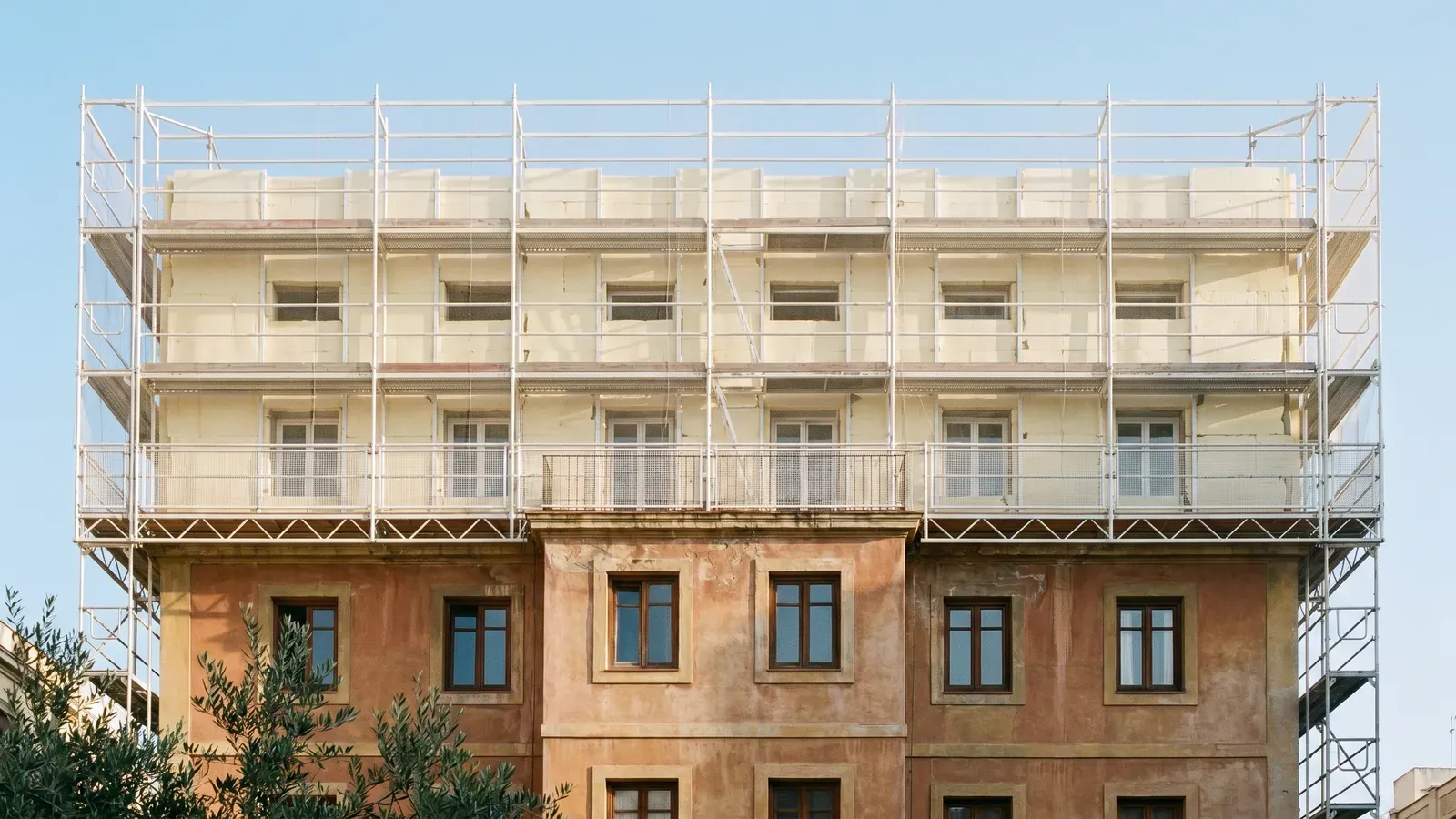 Edificio residencial español en obras de rehabilitación energética con andamios y aislamiento térmico de fachada en la mitad superior, ilustrativo del Plan Estatal de Vivienda 2026-2030 y el Plan Social para el Clima en comunidades de propietarios